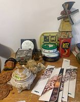 Four vintage tins including a Dutch Mill windmill tin toy which turns (signs of corrosion on the windmill blades), ceramic wall decor, trivets, small tray with animal motifs, and unopened incense sticks. Also seen vintage cast metal woodpecker toothpick dispenser/holder with rust patina.