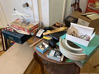 Table with Sony Walkman, puzzle box, Trivial Pursuit game, Concord model airplane, slide carousel, earphones, wooden tool, costume jewelry, and other miscellaneous items.
