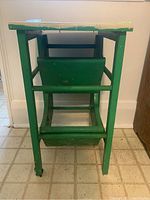 Front view of green painted wooden folding step stool with top surface showing paint wear and chipping.