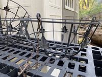 Image showing one metal wrought iron hanging basket holder with circular frame, vertical bars, decorative leaf accents, and attached hanging chain with hook.