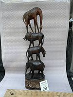 Front full view of stacked carved wooden animals on round carved base showing giraffe, lion, zebra, elephant, and tail damage.