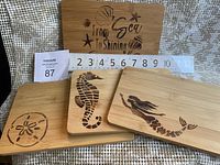 Four bamboo cutting boards shown with wood-burned sea-themed designs including mermaid, seahorse, sand dollar, and a sea phrase. A ruler placed shows length about 9 inches.