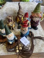 Overall lot showing 6 gnome figurines including three on wooden swing and others around it, placed on woven textile.