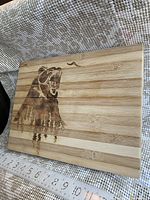 Top view of the bamboo cutting board showing the burnt bear engraving and measuring tape to indicate size.