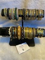 Photo showing two rows of adult preowned bracelets of various styles, including metal bangles and elastic bead bracelets on a stand.