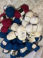 Pile of yarn skeins in deep blue, burgundy, and cream on a textured surface showing the overall assortment and quantity.