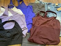 Photo showing assortment of athletic tank tops including black mesh, purple, lilac, burgundy, and brownish-gray, alongside light wash denim jean shorts.