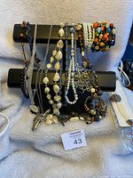 Jewelry displayed on black stand including multiple bracelets and necklaces of various bead and metal designs.