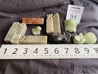 Photo showing seven sculpted soapstone and jade pieces arranged next to a ruler measuring about 9 inches.