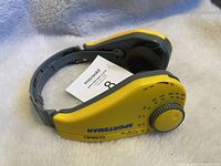 Front and side view of yellow COSMO Sportsman AM/FM radio headphones with adjustable gray headband and foam ear pads on a white fuzzy surface.