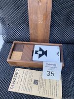 Wooden Tangoes game box with wooden geometric pieces and black and white pattern cards inside. Also showing a folded pattern instruction sheet.