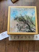 Top view photo showing the wood box with resin top artwork of birds flying over tree branches with a background sky, placed on wooden floor with measuring tape.