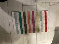Striped multicolor bath mat laid on floor showing color stripes and texture.