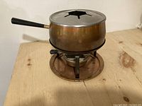 Copper fondue pot with burner and stand on wooden surface.