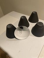 Five small black metal lampshades with conical shape, arranged on a white surface. One visible from inside showing white paint and wiring hole.