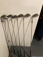 Photo showing seven golf irons with metal shafts and worn steel heads.