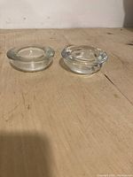 Front view of two solid glass round tea light holders with recessed centers on a wooden surface.