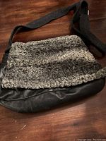 Front view of the courier bag showing black leather base and Persian lamb wool upper edge with grey flannel strap.