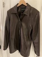 Front view of the brown leather jacket showing collar, long sleeves, button closure, and pockets.