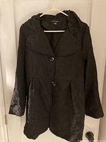 Black long-sleeved women's brocade jacket with subtle floral pattern, button front, and wide collar