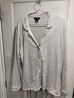 Full view of the pajama top on a hanger showing the button-up front and collar with thin horizontal stripes.