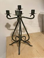 Front and side view of five-arm wrought iron candelabra with noticeable green patina on the metal surface, showing base and candle holders.