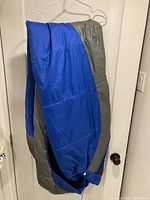 Full view of blue and gray Marmot mummy sleeping bag hanging on a hanger, showing overall shape and color.