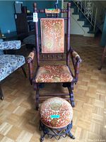 Front view of Victorian wood-framed glider rocking chair with upholstered seat, backrest, and armrests, alongside matching round footstool.