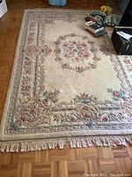 Full view of the beige floral print area rug showing central medallion and fringe edges.