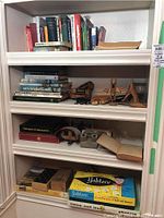 Photo of four shelves containing various vintage and antique books, games, collectibles, and toys including stereoscope, View-Master, pendulum, and books.
