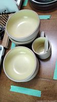 Four pottery bowls and one matching mug arranged on table. Beige interiors and matte natural exteriors visible.