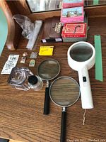 Lot items arranged on a wooden desk including decks of cards, magnifying glasses, pins, ink jars and a screwdriver