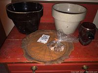 Photo showing two ceramic planters, black and beige, a small ceramic pipe-shaped dish, a carved wooden decorative plate, and a small bag of pennies on a red surface.