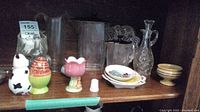 Shelf displaying assorted glass and ceramic items including trays, pitchers, bowls, and decorative items.