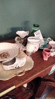 Full view of the assortment of vintage ceramic items on a wooden surface including shaving mugs, teacups, ceramic shoe, and decorative egg.