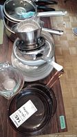 Stack of stainless steel pots and pans topped with an aluminum fluted mold, a glass bowl and a glass measuring cup visible on the side.