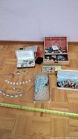 Overview of lot showing necklaces laid out, clear bead box, white jewelry box and wooden compartment box