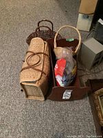 Wooden doll cradle on carpet floor with two wicker purses placed beside it and a small wicker basket inside the cradle storing a plastic bag with unknown contents.