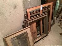 Several vintage wood frames stacked against a basement wall, showing varying sizes and condition.