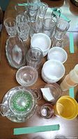 Collection of various drinking glasses, bowls, and plates, including clear and some green-trimmed glass items and Firestone-patterned bowls.