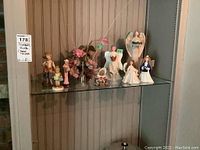 Shelf display of figurines including various angels, a teddy bear, and a floral bouquet.