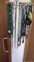 Full view of assorted necklaces and chains hanging on a wooden rack door handle with varied colors and bead types.