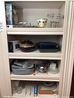 View of shelves showing various kitchenware items including boxed Octo chip and dip set, vintage metal tray, plates, bowls, Pyrex, and food storage containers.