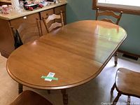 Solid wood dining table with two leaves, oval shape visible, medium brown finish, showing minor scuffs and wear.