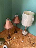 Shows the pair of matching table lamps with bead-trimmed beige fabric shades alongside the taller table lamp with a wider cylindrical shade on a metal and ceramic base.