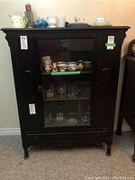 Front view of vintage wood cabinet with glass door showing decorative molding and contents inside.
