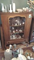 Front view of vintage solid wood display cabinet with glass door showing contents inside and dovetailed drawer at base