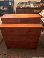 Photo of a light tan wooden dresser with five drawers, placed in a room with other furniture items around.