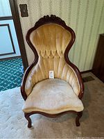 Vintage accent chair with curved wooden frame and beige velour upholstery shown from front view.