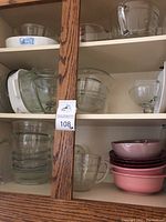 Shelf of assorted clear glass mixing and salad bowls, some with handles, and stacked pink ceramic bowls.